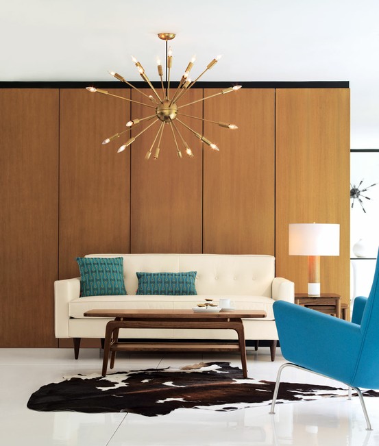 a simple and neutral living room with a plywood covered wall, a sunburst chandelier, a creamy sofa and a blue chair plus matching pillows