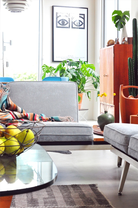 a bright mid-century modern living room with grey furniture, a wooden cabinet, potted greenery and cacti and lamps