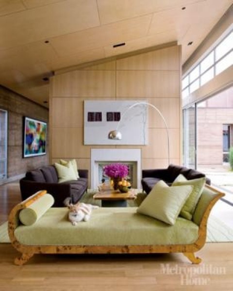 a bright mid-century modern living room with plywood walls and ceiling, dark furniture and a green couch with lots of pillows