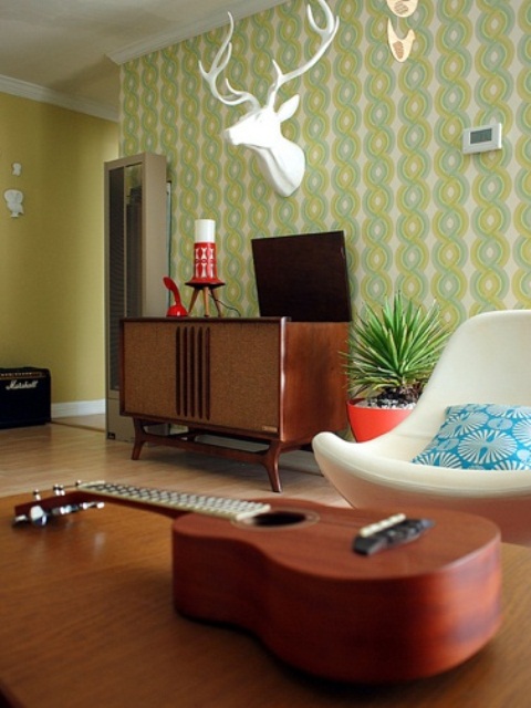 a mid-century modern living room with green printed wallpaper, elegant dark stained furniture and a faux animal head