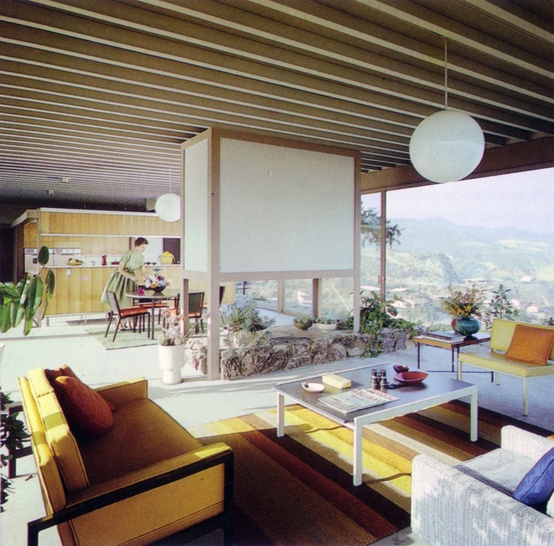 a neutral mid-century modern living room with yellow furniture, lots of greenery and a large panoramic view