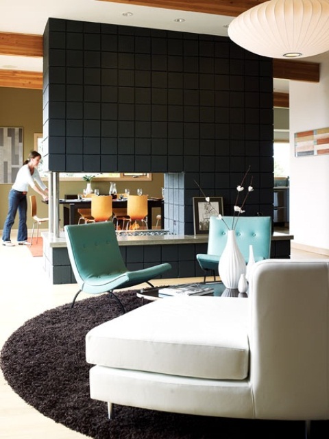 a mid-century modern living room with white and blue furniture and a dark tiled fireplace that divides the spaces