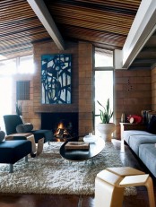 a mid-century modern living room with large bricks, navy and grey furniture, a fireplace and an abstract artwork