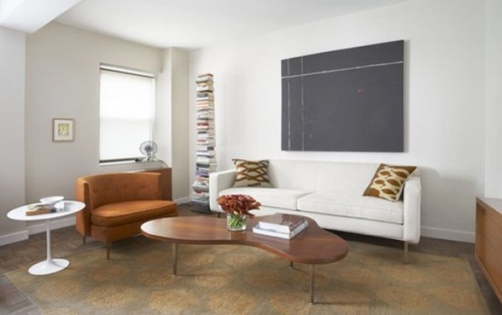 a neutral and airy living room with brown furniture, a creamy sofa, a stack of book and an artwork