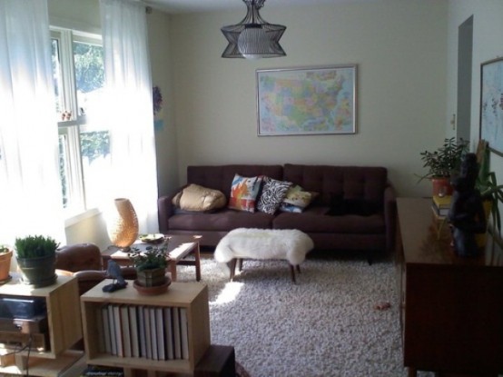 a small and neutral living room with a dark sofa and chair, a fluffy rug and stool and a chandelier