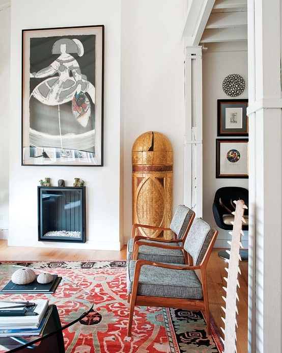 a mid-century modern living room with a printed rug, artworks and a built-in fireplace and cozy chairs