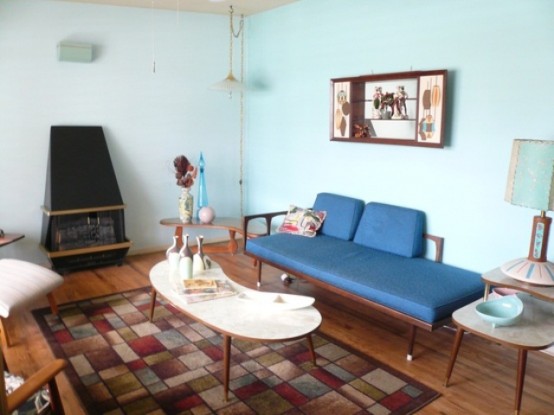 a quirky mid-century modern space with a blue couch, a printed rug, a heart and some unusual lamps