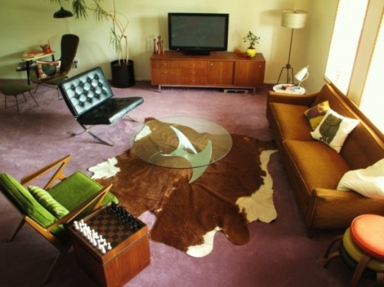 brown and light green living room with a faux animal skin, bright pillows, green chairs and a plywood TV cabinet