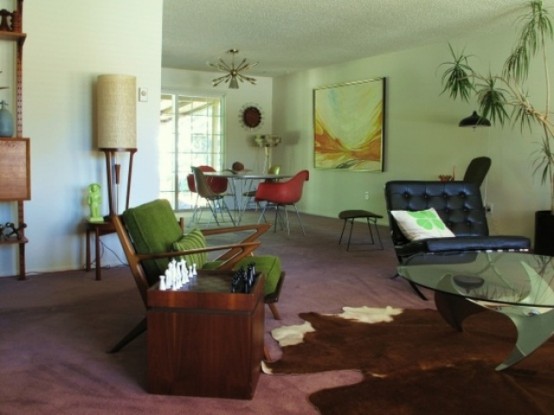 a pastel grene mid-century modern living room with dark stained furniture, potted greenery, artworks and lamps