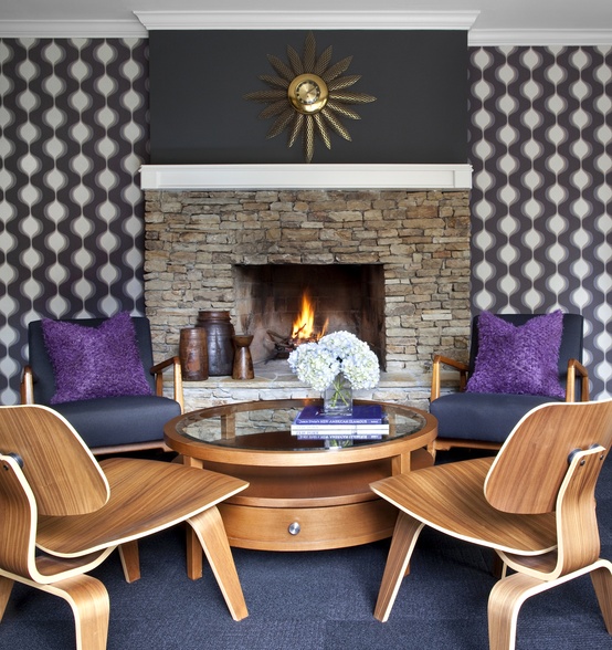 a mid-century modern living room with a built-in fireplace, printed wallpaper and catchy plywood furniture and a sunburst clock