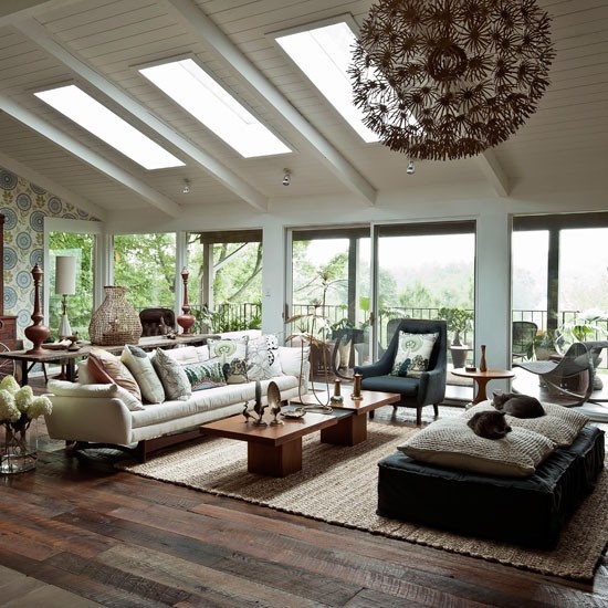 a cozy boho meets mid-century modern living room with dark and neutral furniture, skylights, wooden tables and much natural light