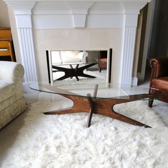 a refined mid-century modern coffee table with a beautiful rich-stained wooden base with legs and a clear glass oval tabletop is chic