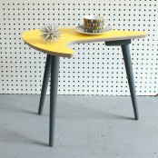 a Scandinavian mid-century modern coffee table on tall grey legs and with a curved and creatively-shaped yellow countertop will make a statement with both its color and shape