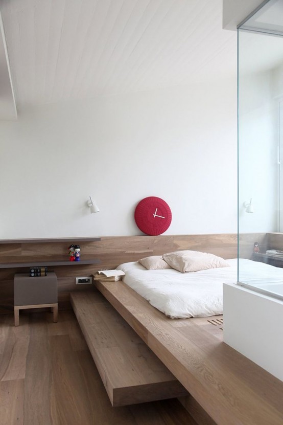 a minimalist bedroom with a platform bed with steps, a small nightstand and a red clock, a shower right in the room