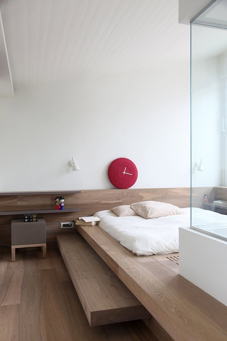 a minimalist bedroom with a platform bed with steps, a small nightstand and a red clock, a shower right in the room