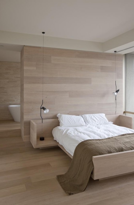 a natural minimalist bedroom with a glazed wall, a space divider and a bathroom behind the wall, a light-stained bed and neutral bedding
