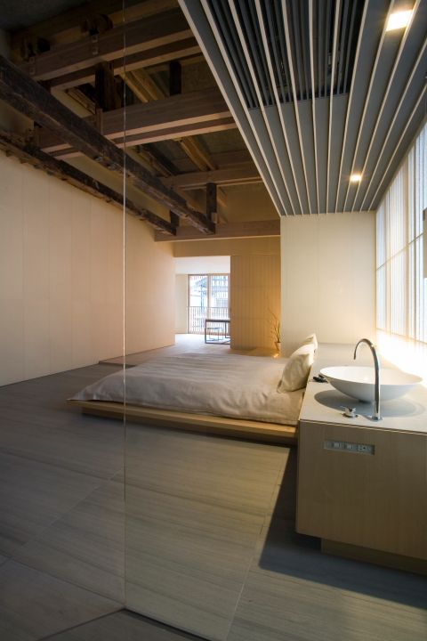 an airy minimalist bedroom with a platform bed, a large vanity with a sink, lights, a large window and a lot of negative space