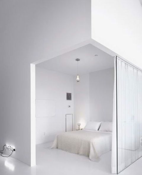 a crispy white minimalist bedroom with a white bed and bedding, pendant and table lamps and a glass space divider with curtains