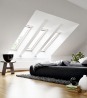 a contemporary meets minimalist bedroom with a black bed, grey and white bedding, skylights and potted greenery is very welcoming
