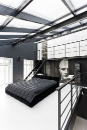 a minimalist meets industrial bedroom with a black bed and grey bedding, a statement artwork and a glass ceiling to maximize natural light