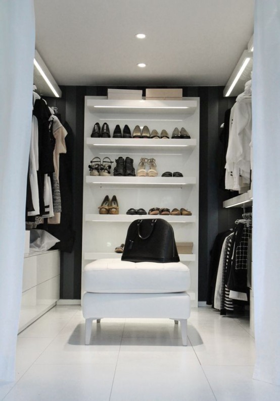 a minimalist black and white closet with hangers, open shelving and some sideboards plus lights