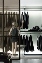 a minimalist closet done with lots of holders, built-in lights and separated from the rest of the space with a glass sliding door