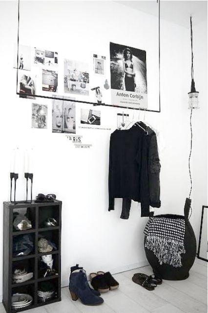 a minimalist closet with a holder for hangers, a black storage unit, a basket and a pendant lamp over it all