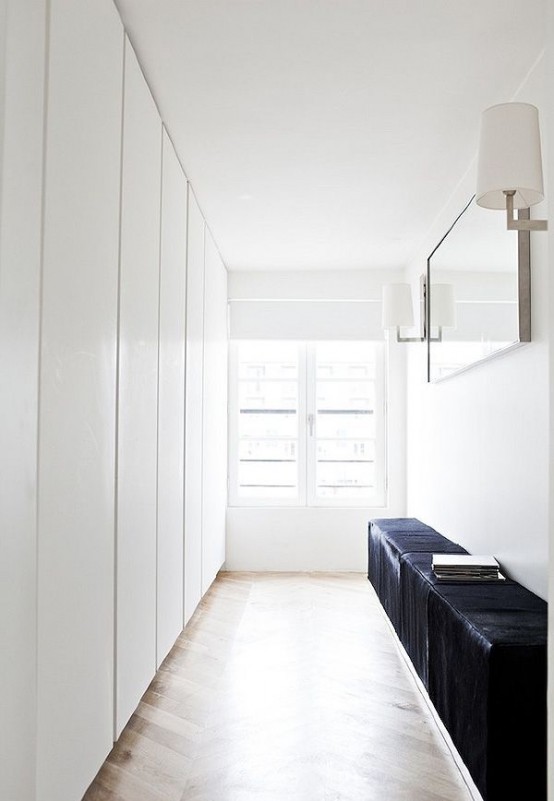 an ultra-minimalist closet with lots of wardrobes done in white, with sleek panels and a black leather bench