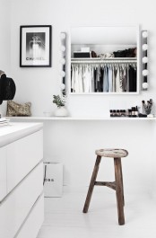 a minimalist makeshift closet in white, with some sleek dressers, a cozy makeup nook and a comfy stool