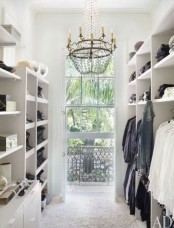 a minimalist open closet in white, open shelving and a large window to fill the space with light and a glam chandelier to add chic