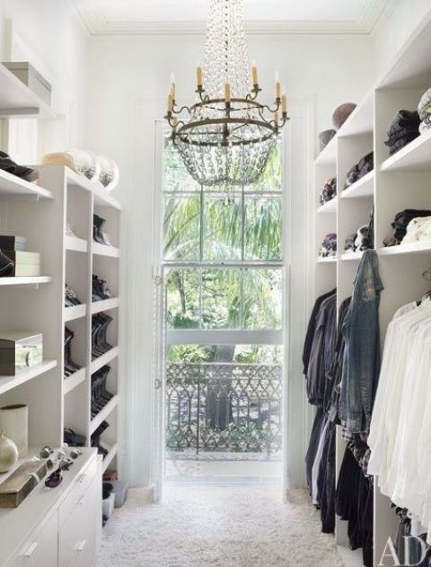 a minimalist open closet in white, open shelving and a large window to fill the space with light and a glam chandelier to add chic