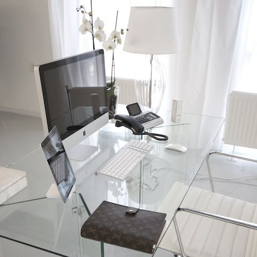 a sophisticated minimalist home office with a clear glass desk, a white chair, a floor lamp and some gadgets is an ultimate workspace