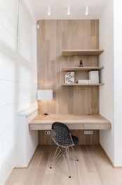 a minimalist home office nook clad with wood, with several shelves, a built-in desk and a black chair plus some lights for comfortable working