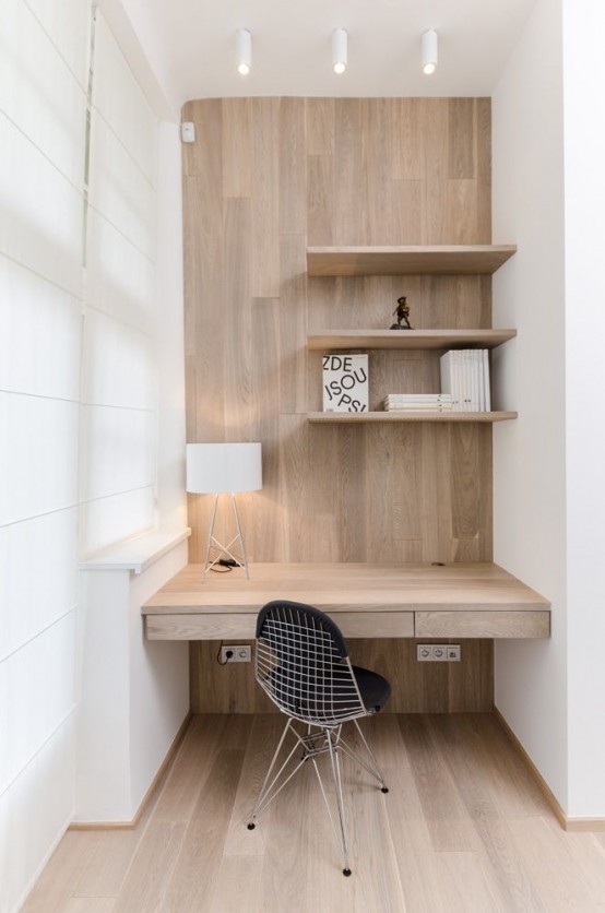 a minimalist home office nook clad with wood, with several shelves, a built-in desk and a black chair plus some lights for comfortable working