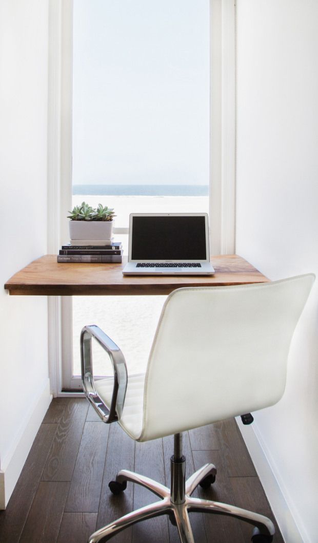 a minimalist home office with a sea view, a built in desk, a white chair, a stack of books and a potted plant is very sleek and cool