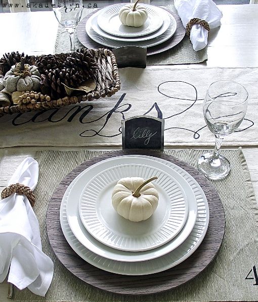 a neutral Thanksgiving tablescape with a neutral table runner, placemats, a basket with pinecones and berries, chalkboard tags