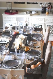 a modern Thanksgiving table setting done in greys, metallic and black, pillar candles and gourds in a basket