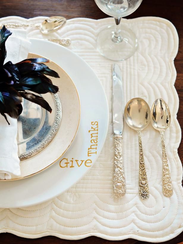 a modern refined place setting with an embroidered placemat, elegant plates and gold cutlery and a black feather arrangement