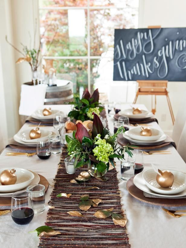 a modern fall or Thanksgiving tablescape with a stick and foliage table runner, brown chargers, gilded apples and dark floral centerpieces