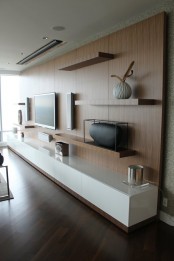 a modern and sleek white TV unit, some floating shelves all attached to a single piece that takes a whole wall