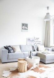 a neutral modenr light-filled living room with a grey sectional, mismatching pillows, a cowhide rug and a tree stump, a pendant lamp