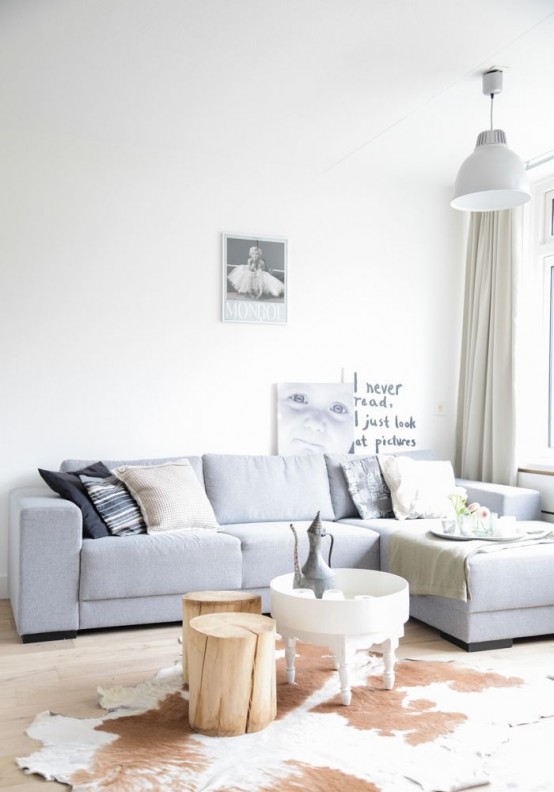 a neutral modenr light-filled living room with a grey sectional, mismatching pillows, a cowhide rug and a tree stump, a pendant lamp