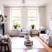 a refined vintage neutral living room with a fireplace wiht a dark mantel, neutral seating furniture, potted plants, dark touches for more drama