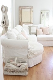 a neutral shabby chic living room with grey walls, a white sectional, neutral mismatching pillows, vintage doors and a clock, a basket for storage