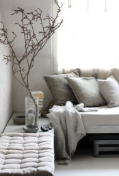 a very neutral wabi-sabi living room with a concrete bench, textural pillows and a blanket, a bench and some branches in a clear vase