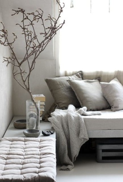 a very neutral wabi sabi living room with a concrete bench, textural pillows and a blanket, a bench and some branches in a clear vase
