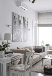 a neutral Scandi living room with tan and creamy furniture, white dining furniture, a statement artwork and a dark coffee table