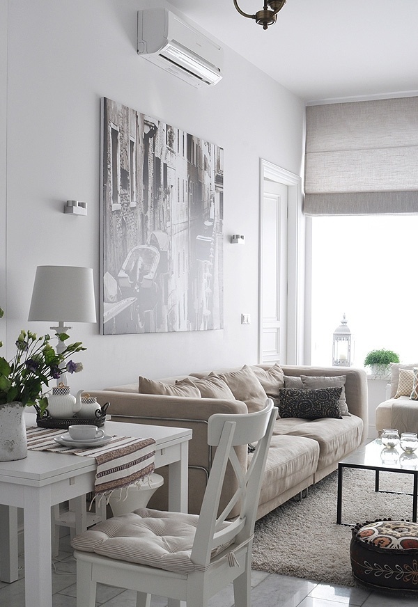 a neutral Scandi living room with tan and creamy furniture, white dining furniture, a statement artwork and a dark coffee table