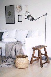 a neutral living room with a white sofa, white pillows and blankets, a metal floor lamp, a wood stool and a small gallery wall