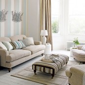 a cozy neutral living room with striped walls, neutral furniture, a striped ottoman and a striped rug is a lovely light-filled space